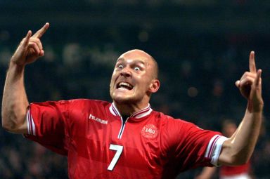 Danish footballer Thomas Gravesen, a shaven headed man, pulls a scary facial expression - eyes wide open, mouth open and his hands shaped like devil horns. He is celebrating scoring a goal for Denmark after a football game.