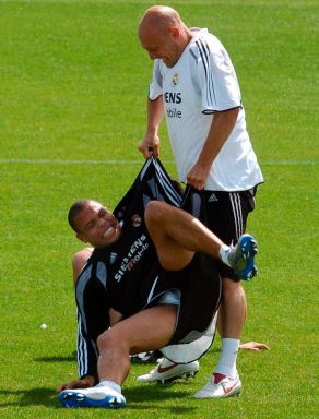 Footballer Thomas Gravesen, wearing a white T-shirt, pulls his Real Madrid teammate Ronaldo, wearing a black T-shirt and shorts, off the grass. The two are having a rough training session in Spain.