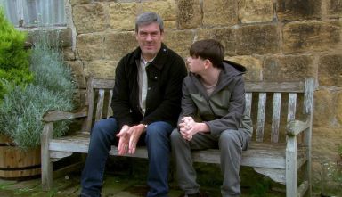 Cain and Kyle sit on a bench outside the wishing well cottage 